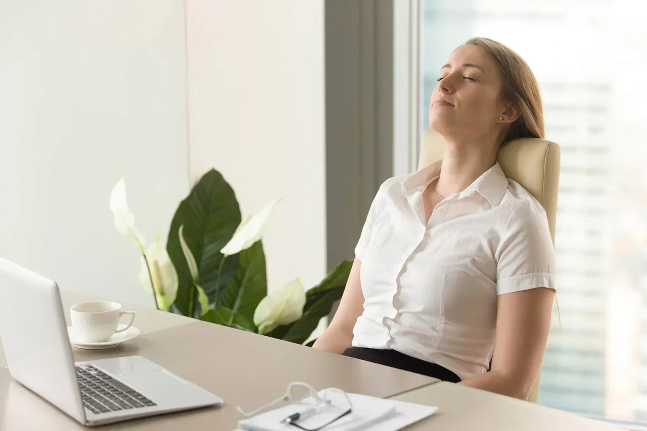 Relaxed businesswoman enjoying fresh air at modern office desk with laptop, coffee, and indoor plant