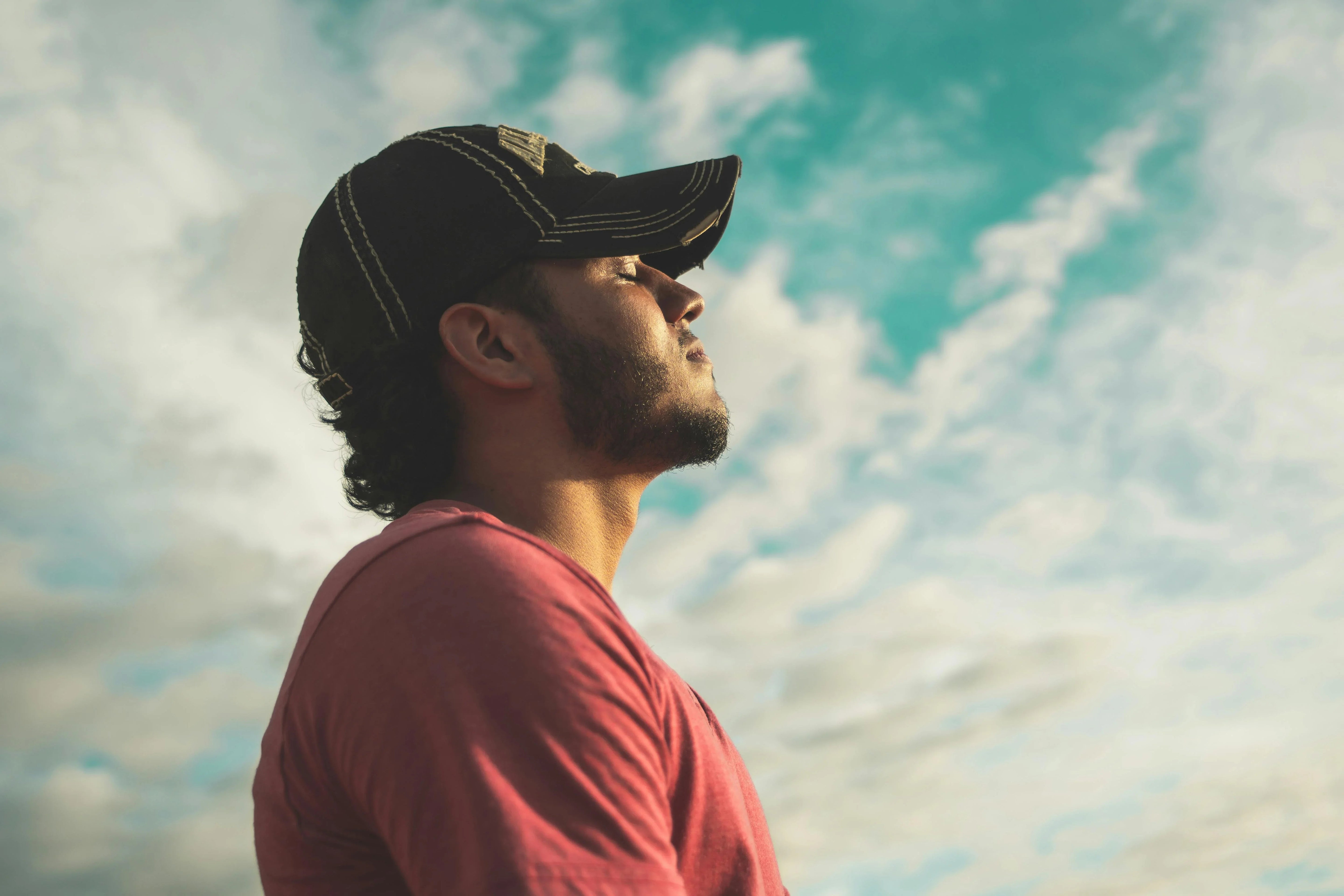 Man in casual shirt and cap relaxing outdoors under blue sky with soft clouds